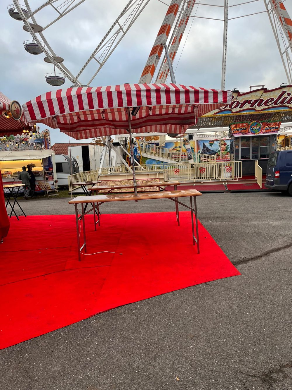 Bierbank unter gestreiftem Schirm, dahinter ein Riesenrad und Fahrgeschäfte