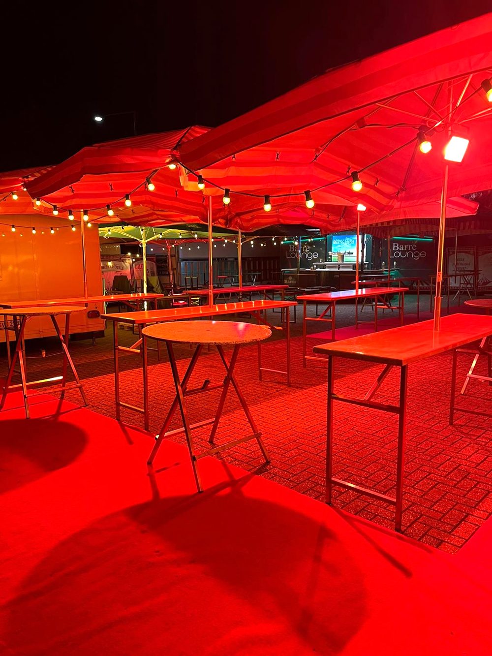 Rote Schirme mit Lichterkette über den Tischen bei Nacht